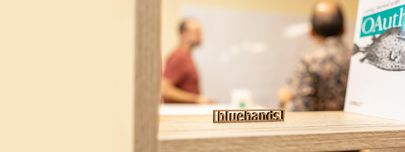 Kontakt – Viele Wege führen zu bluehands Holzschriftzug 'bluehands' in einem Regal, im Hintergrund unscharfe Personen