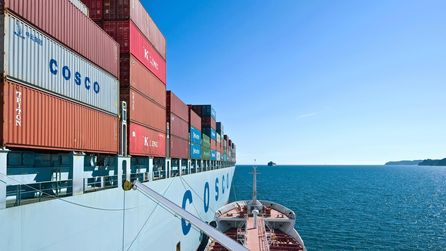 Ein großes Containerschiff, an der Seite hat ein kleineres Boot angelegt